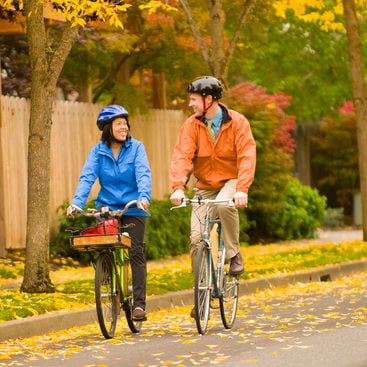 photo of man and woman biking through autumn leaves