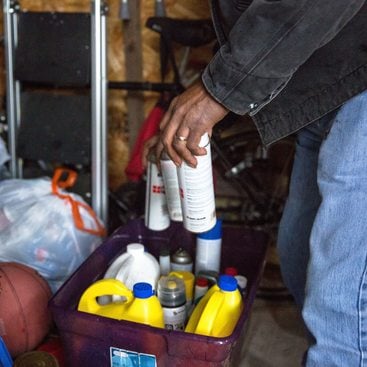 aerosol cans being placed in a recycling bin inside a garage