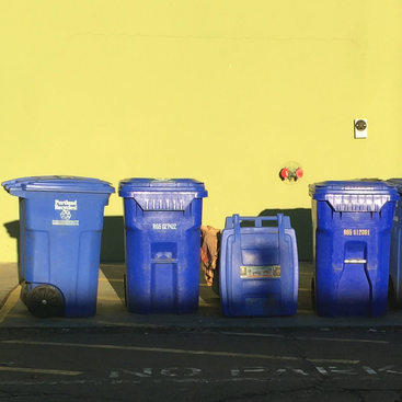 blue recycling bins against a yellow wall