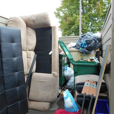 couch and other furniture in recycling area alongside recycling bins and dumpster