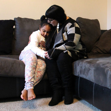 A portrait of Dawn Swan sitting in her living room with her daughter