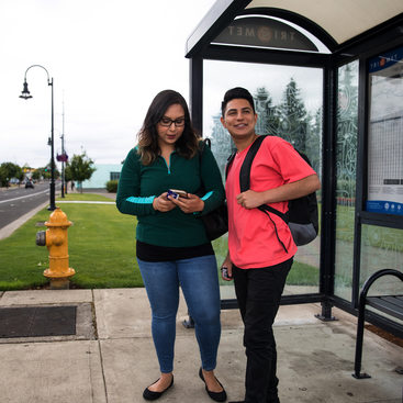 Two people, a young man and woman, wait at a bus stop.