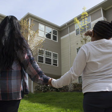 woman and daughter holding hands and looking at an apartment building