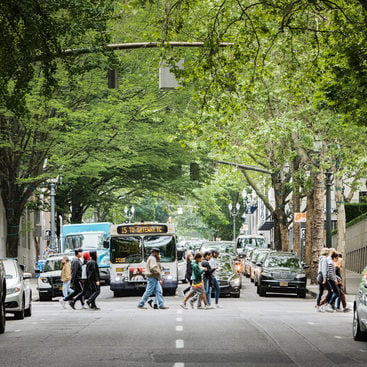 pedestrians cross the street in front of a bus on a street lined with parked cars