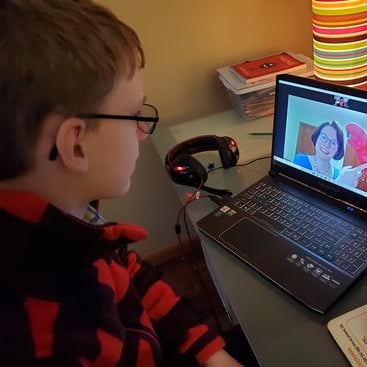 A young child attends an online distance learning program hosted by a Metro educator from his laptop on a desk at home