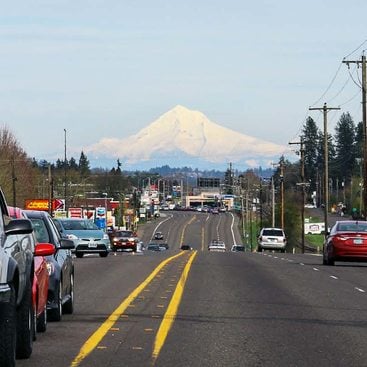 A view of Southwest Tualatin Valley Highway looking east, with a snow-covered Mount Hood in the distance and heavy traffic on the road.