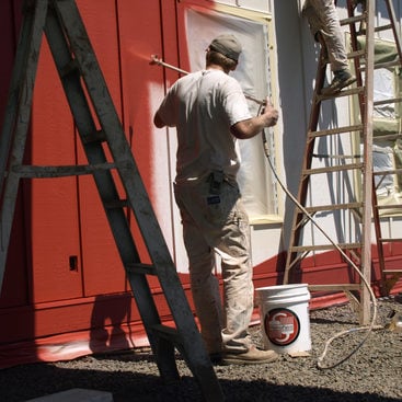 An image of two people painting a house red