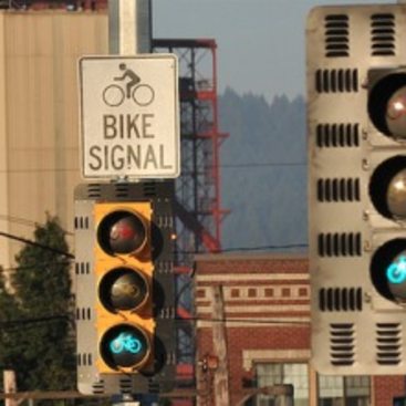 Two different traffic signals for bicycles showing an illuminated green bike symbol in the signal, next to a white informational sign that reads "bike signal."