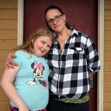 Woman in black and white plaid shirt with her arm around a young girl in a blue shirt with Minnie Mouse on it.