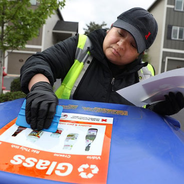 a woman uses a plastic tool to scrape air bubbles out a decal on top of a recycling bin