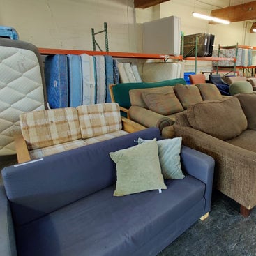 interior of a warehouse with couches in the foreground and mattresses in the back