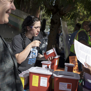 Three people gather around a table full of red medical sharps disposal boxes