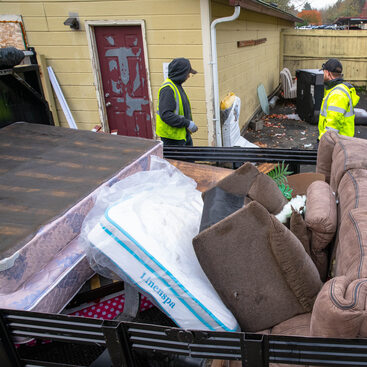 Overhead view of full trailer hall with couches and other furniture while waste management haulers collect more discarded items in an apartment complex.