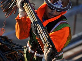 a construction worker carries a bundle of metal rebar at a construction site