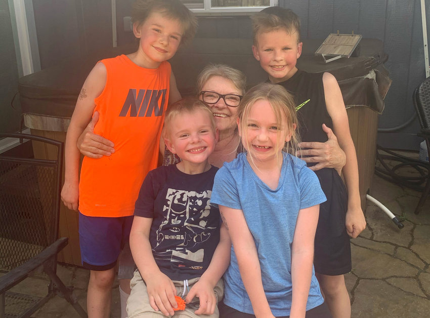 A family photo, taken outside a manufactured home, of a seated woman surrounded by four smiling grandchildren.