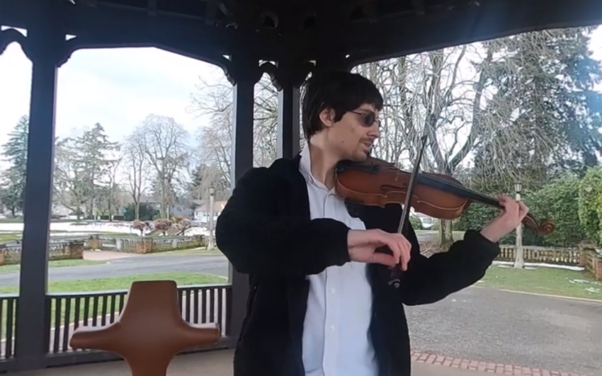 screenshot from film with youth playing violin at a park under a gazebo