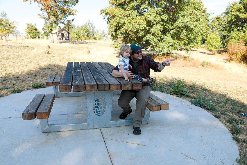 An adult sits at a picnic table with a toddler and points to something in the distance.