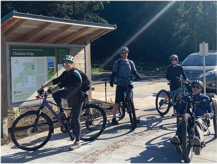 Four mountain bikers pose for a photo around a map of Chehalem Ridge Nature Park.