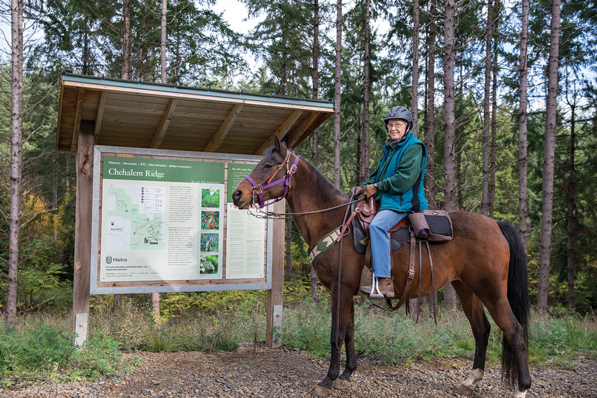A horse and rider stand next to a map with trees behind them.