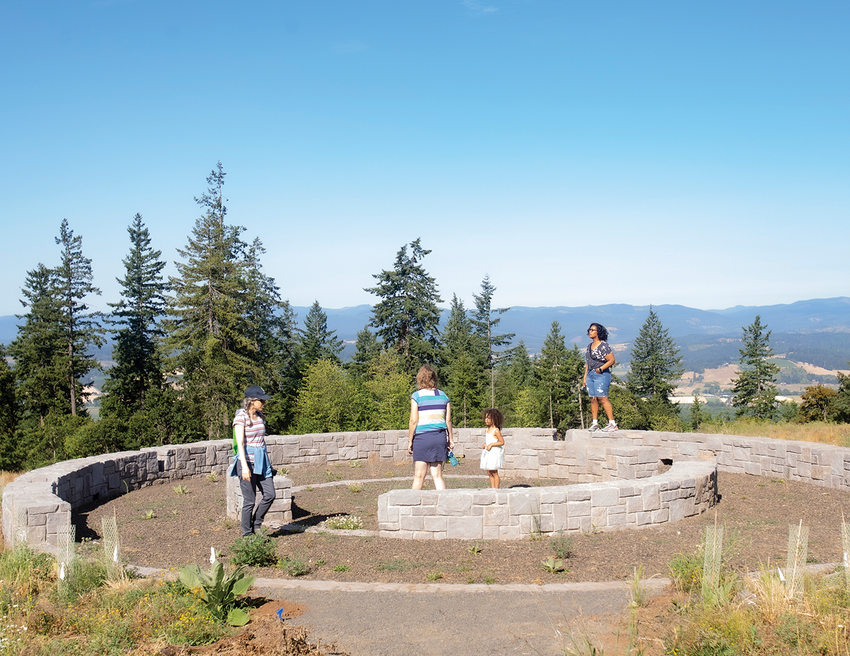 A group of visitors, including kids, stand in a large stone circle that provides seating at an overlook with views of the Coast Range and Tualatin River Valley.