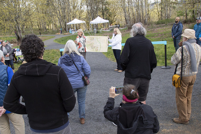 Two women hold a map between them in front of a small crowd.