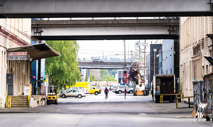 A view down an industrial neighborhood with warehouses lining a street and bridge overpasses above the buildings.