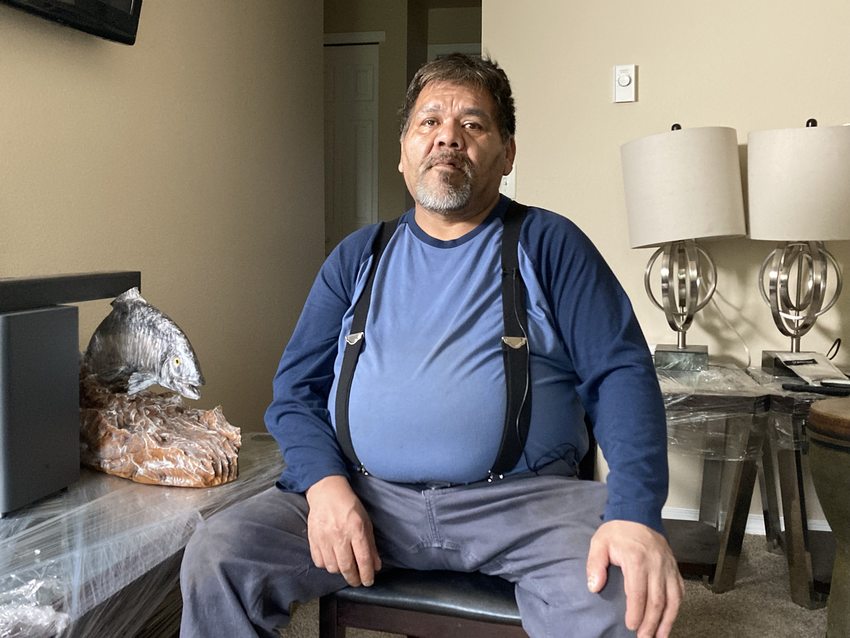 Native American man sitting in living room with a fish sculpture on one side and two lamps on the other