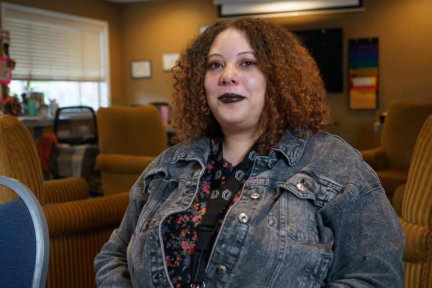 Woman with curly red hair, denim jacket and black lipstick sitting in office