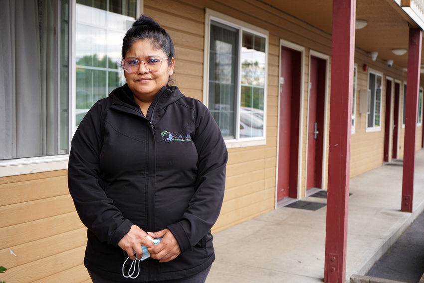 Latina women in black jacket stands in the exterior corridor of a motel