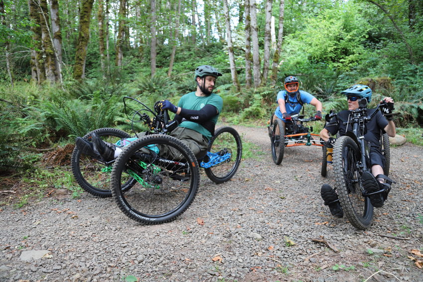 three adaptive mountain bikers stopped on a dirt trail to chat