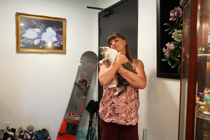 Woman in a pink blouse holding a cat, with a snowboard and several pieces of art behind her