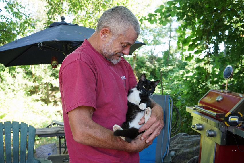 Man in red shirt with short grey hair cradling black and white cat
