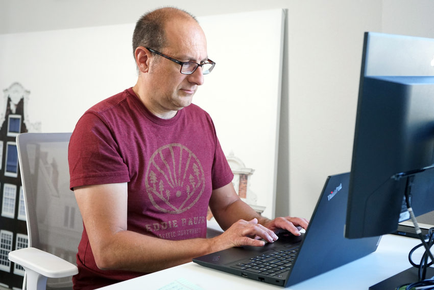 Man in maroon shirt with glasses sitting at computer and typing on keyboard