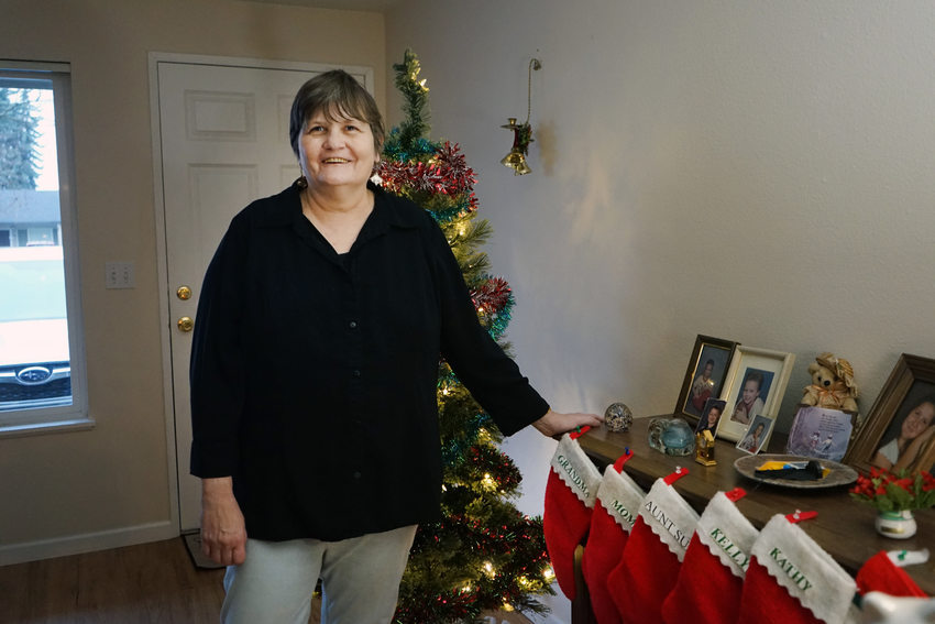 Woman with short hair in black shirt in front of Christmas tree. Her hand is resting on a table with Christmas stockings hanging off the edge.