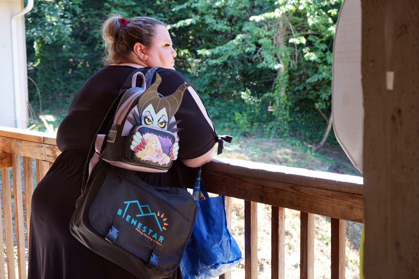 Woman standing at wooden railing and looking over side into the distance. She's wearing a black dress and is carrying several bags.