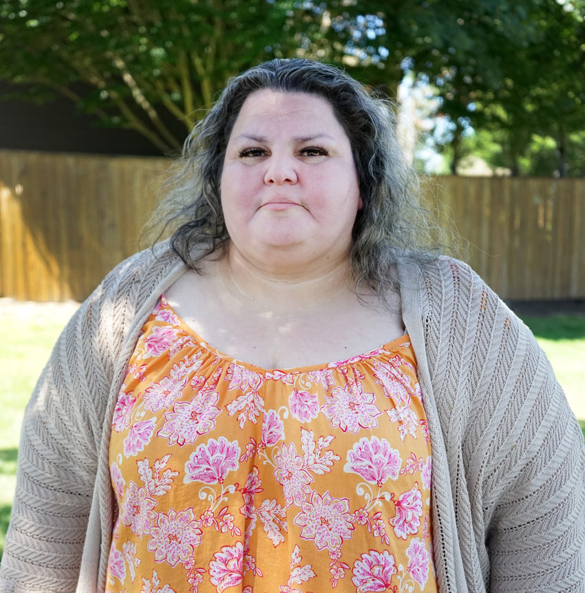 Portrait of a woman in a park setting with an orange and pink floral dress and beige cardigan