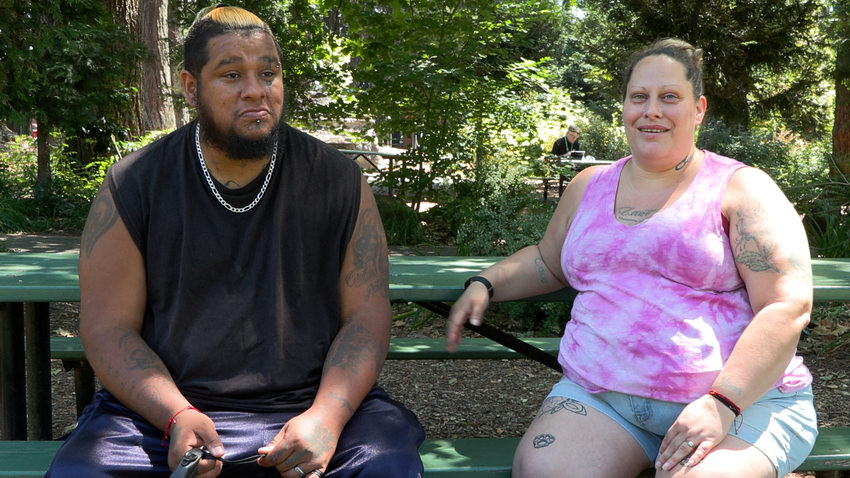 Man with a black shirt sitting next to woman in a pink tank top at a picnic table in the park