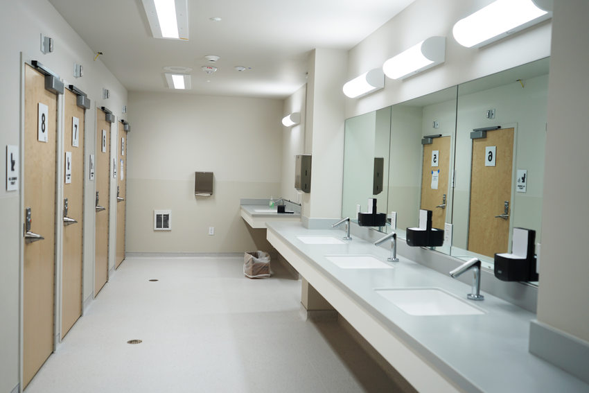 Group restroom with multiple stall doors and sinks, in bright white lighting