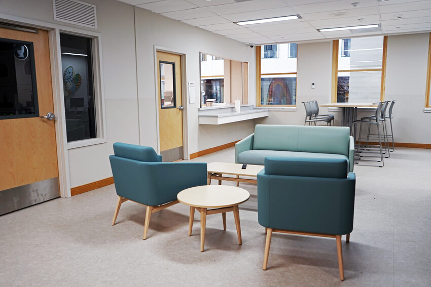 Lounge area with blue stuffed chairs in the foreground an hightable in the background, in fron of windows