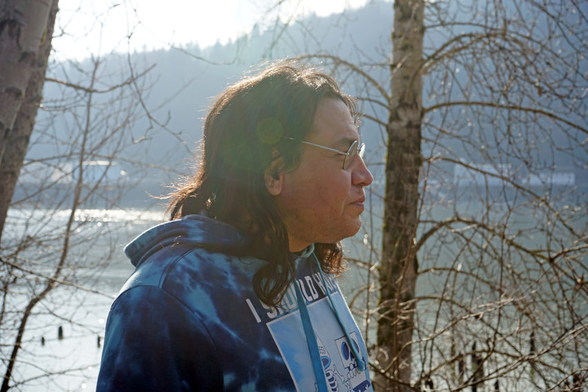 Close up in profile of man in blue hooded sweatshirt standing by a river