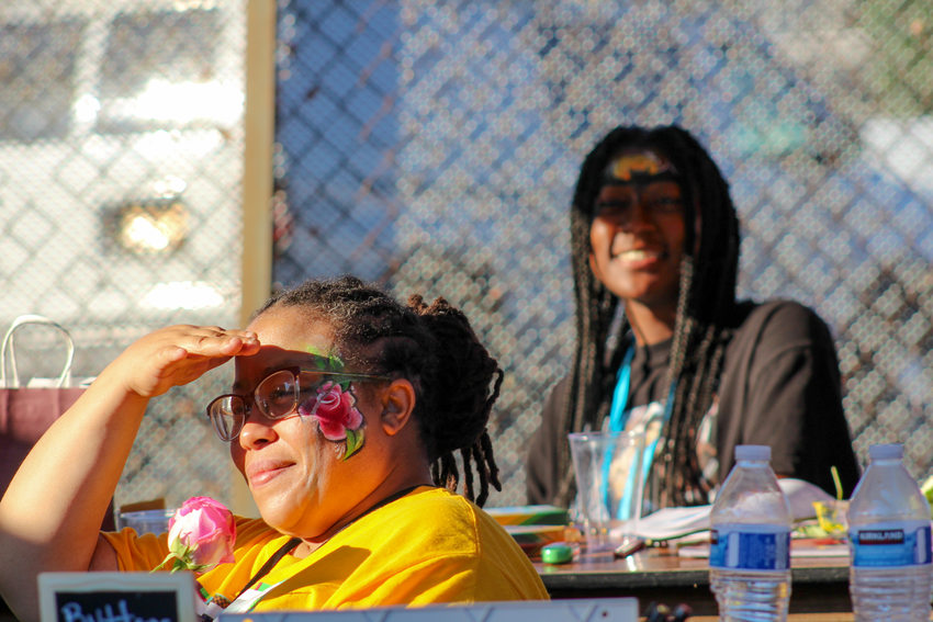 Poet La Toya Hampton shades her face from the sun at her booth at Afro-topia while her youth mentee smiles in the background