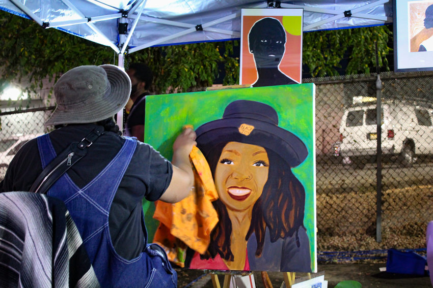 A painter uses a cloth to touch up a portrait she is working on beneath a tent at the Afro-topia pop-up event