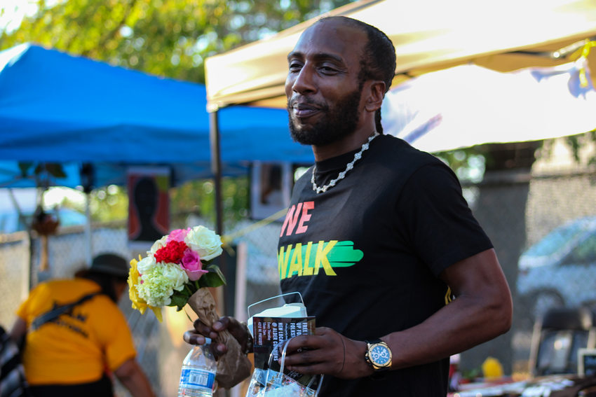 A Black man smiles with flowers and goods from vendors at the Afro-topia pop-up event