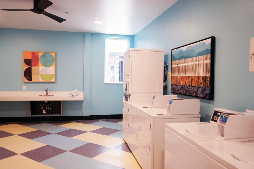 Laundry room with blue walls, colorful flooring and paintings.