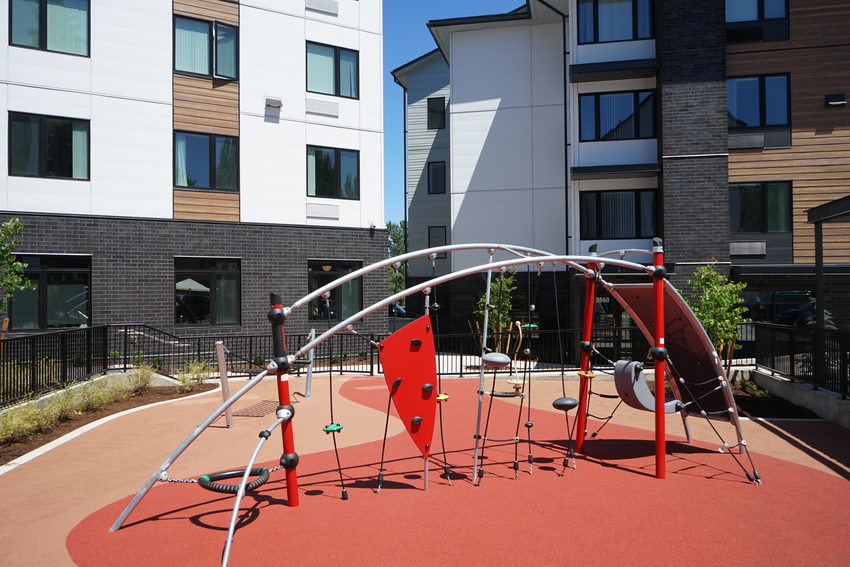 Playground structure on red turf surrounded by multistory apartment buildings.