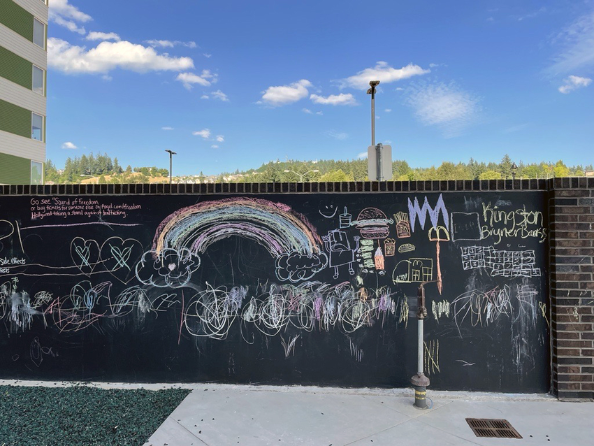 Chalkboard wall with colorful chalk drawings adjacent to a multistory apartment building