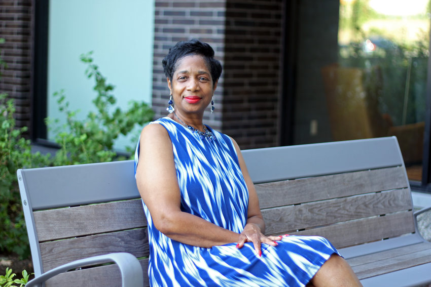 Woman with short dark hair and a blue print dress sitting on a bench