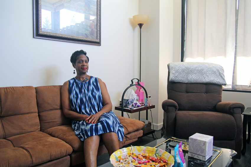 Woman with short dark hair and a blue print dress, sitting on a sofa in her apartment