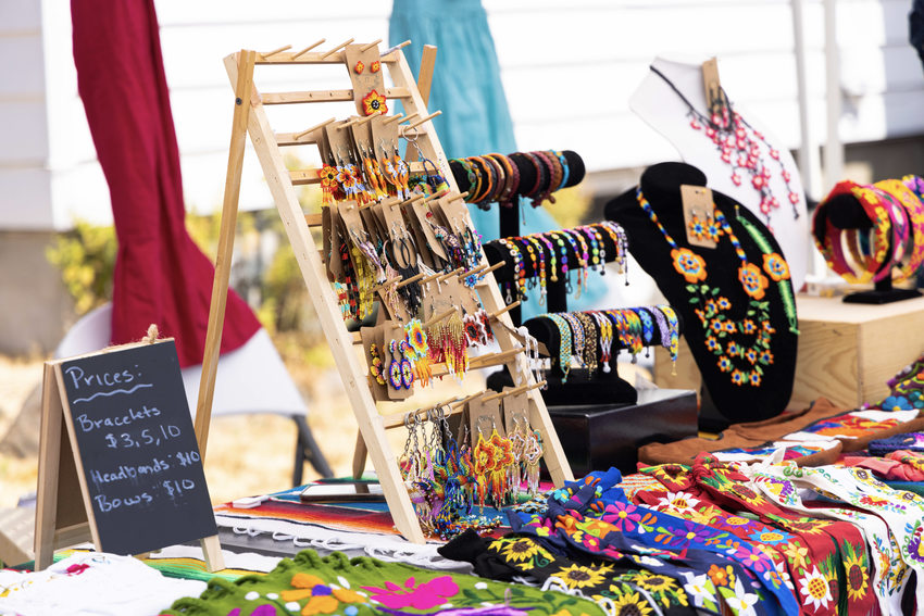 A table displays brightly colored hand embroidered ties and tote bags, and vibrant hand beaded jewelry.