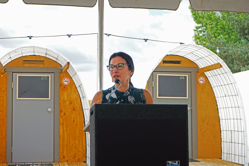 Woman speaking at a podium with two small structures behind her.